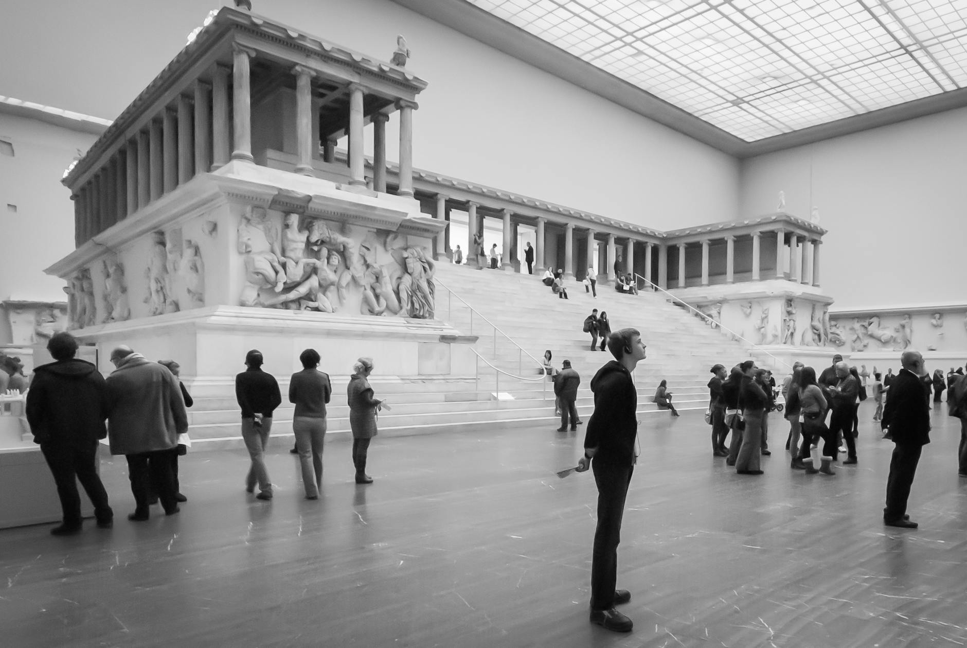 Black and white photo of people exploring an ancient Greek exhibit indoors.